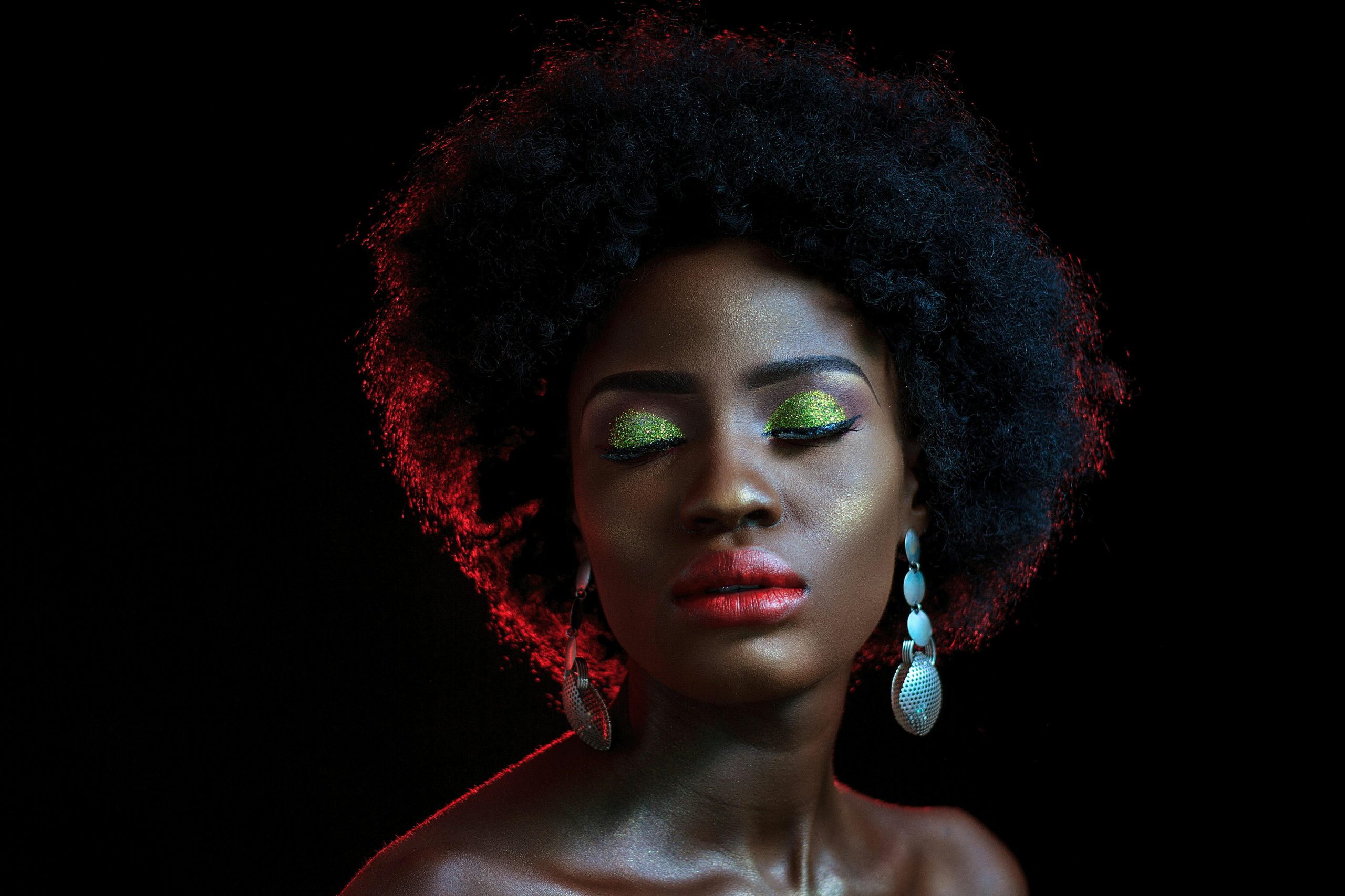 Home Elegant portrait of a woman with afro hair, vibrant eyeshadow, and red lips.