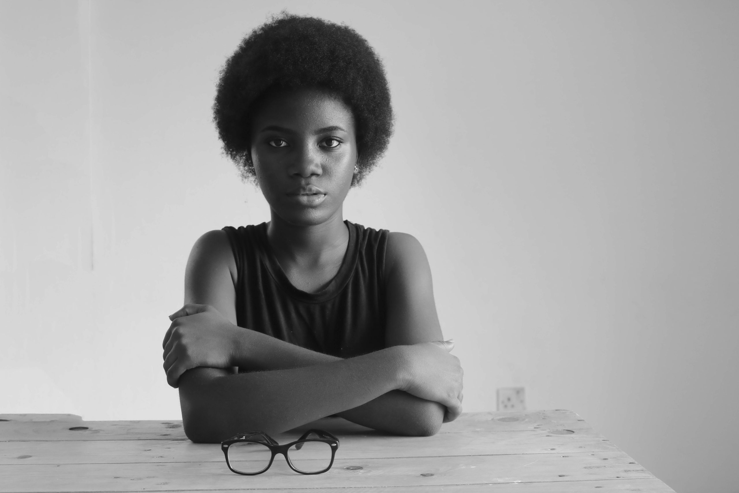 Home Striking monochrome portrait of a woman with afro hair seated at a table.